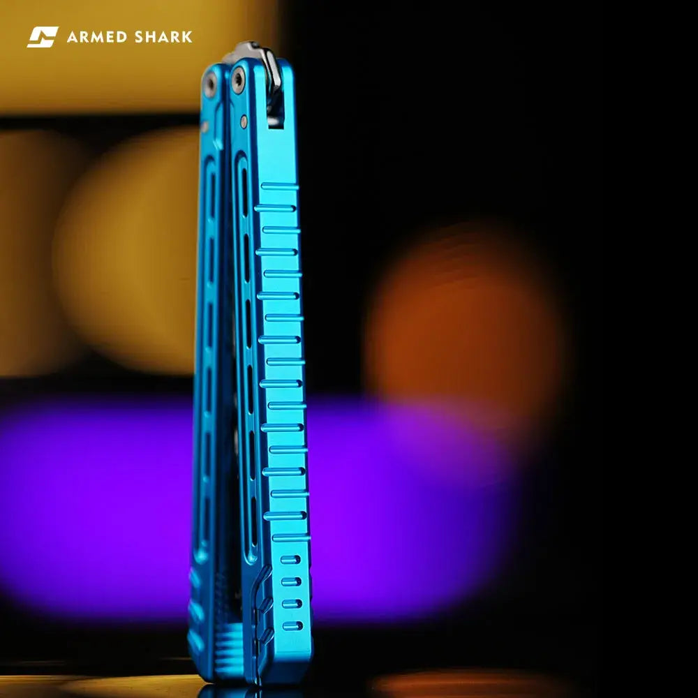 Armed Shark Athena Balisong Trainer in anodized blue finish, closed position showing precision-milled tail grooves and CNC-machined handle texture