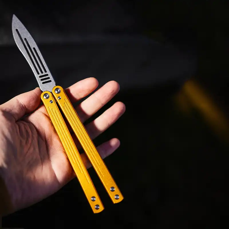 Armed Shark Balisong Trainer with gold handle shown in hand – flipping trainer tool.
