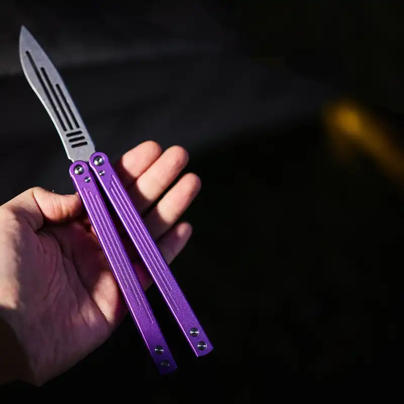 Armed Shark Balisong Trainer with purple handle held in hand – outdoor view.