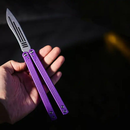 Armed Shark Balisong Trainer with purple handle held in hand – outdoor view.
