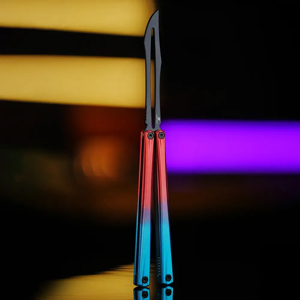 Front view of Armed Shark Eureka Balisong Trainer in red-blue gradient anodized handle with stonewashed training edge, displayed under warm yellow and purple lighting for a vivid contrast