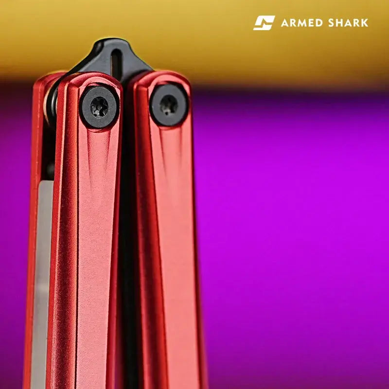 Close-up of Armed Shark Eureka Balisong Trainer red anodized handle showing precision T10 pivot screws and smooth CNC-machined chamfers under studio lighting