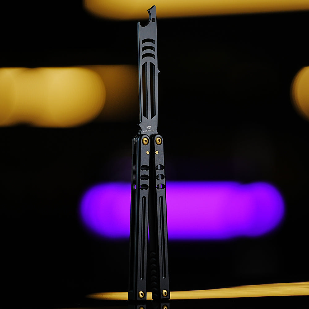 Armed Shark Inked Mako bottle-opener balisong trainer with black training edge and black handles with gold hardware, front view, studio background.