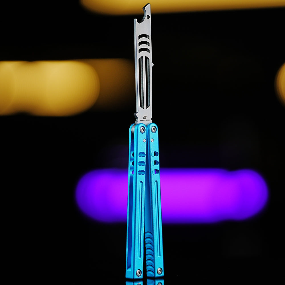 Armed Shark Inked Mako bottle-opener balisong trainer with silver training edge and blue handles, front view, studio bokeh background.