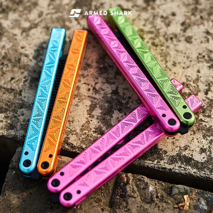 Colorful Armed Shark Original Balisong Trainer handles in pink, green, orange, and blue on outdoor stone surface.