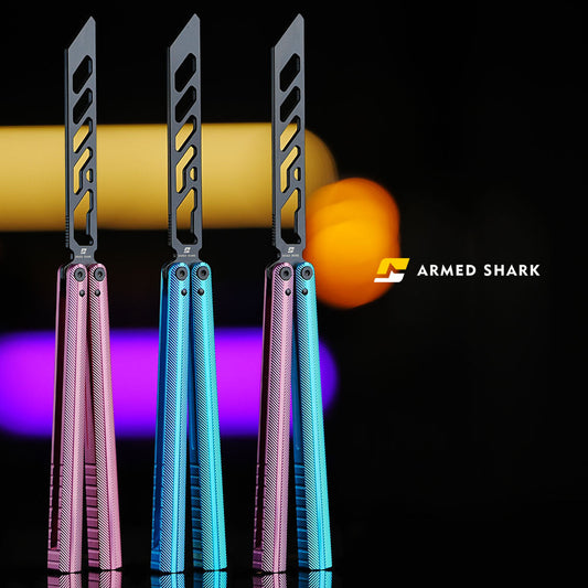Three Armed Shark Pacific Ocean Balisong Trainers in pink, blue, and pink-blue gradient anodized finishes, featuring stainless training edges and 7075 aluminum handles, displayed under warm yellow and purple lighting with brand logo