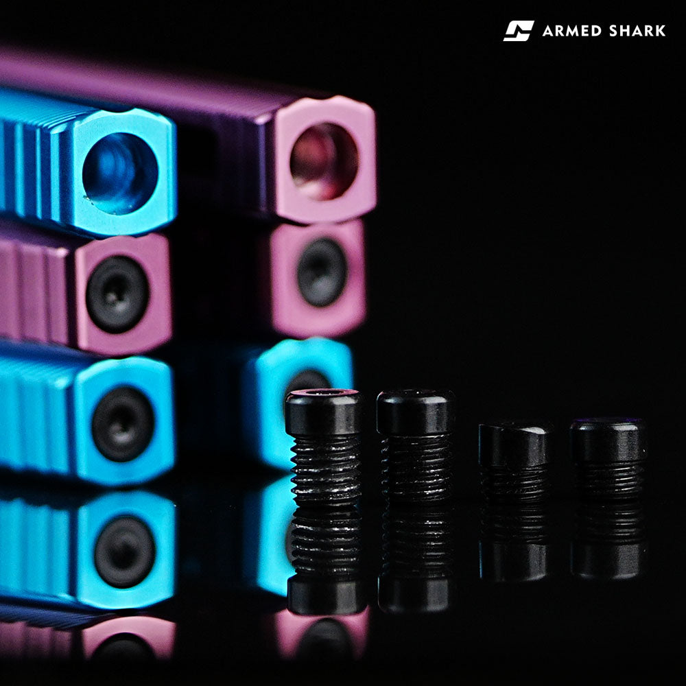 Close-up view of Armed Shark Pacific Ocean Balisong Trainer handle ends in pink and blue anodized aluminum with T10 precision screws displayed on reflective black surface