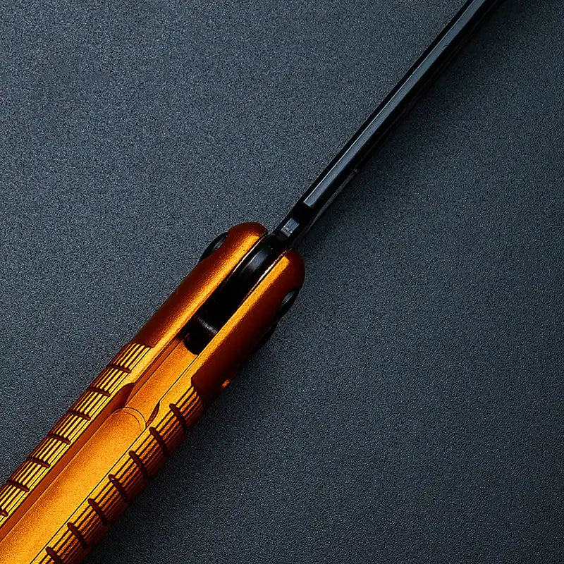 Pivot close-up of Armed Shark Sahara Butterfly Trainer with orange aluminum handle and black training edge